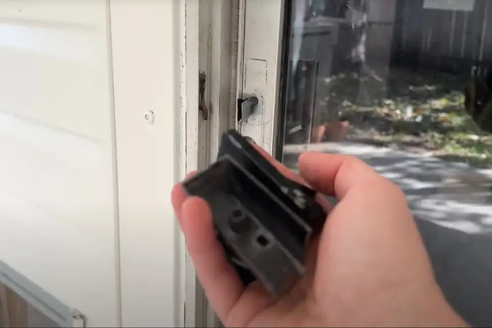 A hand holding a worn tandem roller assembly removed from a patio door panel
